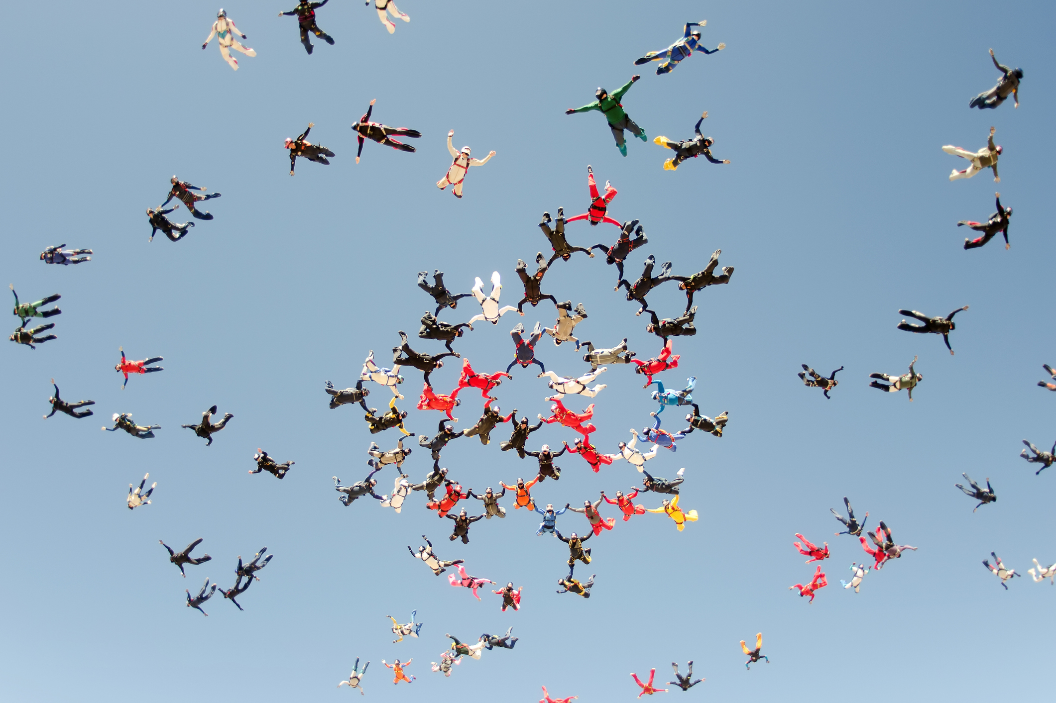 a scattered group of sky divers in different colors begin to form a group mid-air