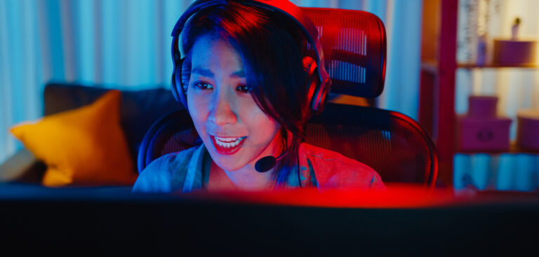 Close-up face happy asia professional girl gamer wear headphone competition play video game neon light computer in living room at home. Esport streaming game online, Home quarantine activity concept.