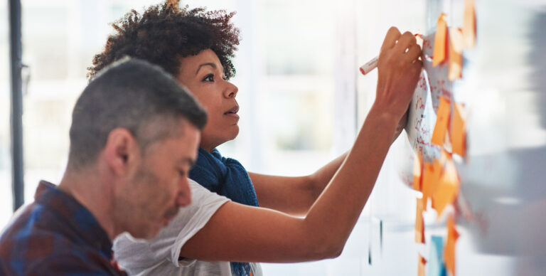 A businessman and businesswoman brainstorming on a whiteboard in a tech start-up office