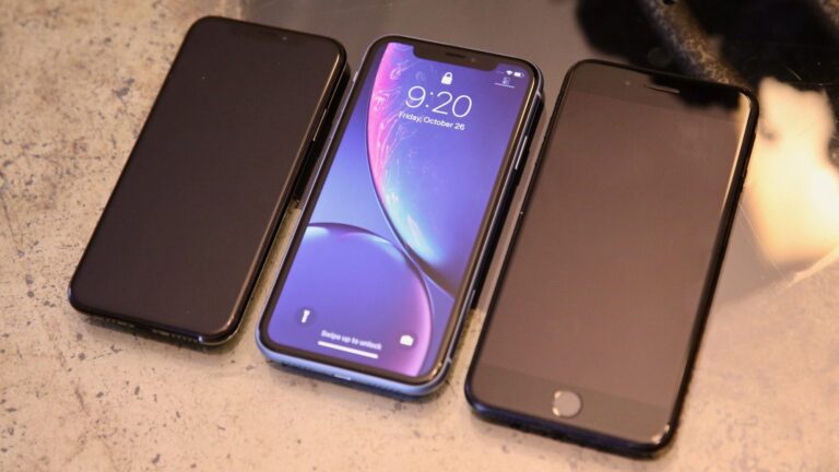 The iPhone XR sits between the iPhone XS (left) and an iPhone 7 Plus (right).