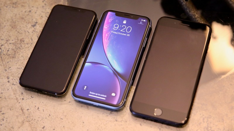 The iPhone XR sits between the iPhone XS (left) and an iPhone 7 Plus (right).