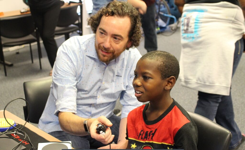 Mark Barlet of AbleGamers shows a child how to play video games using an inclusive controller.