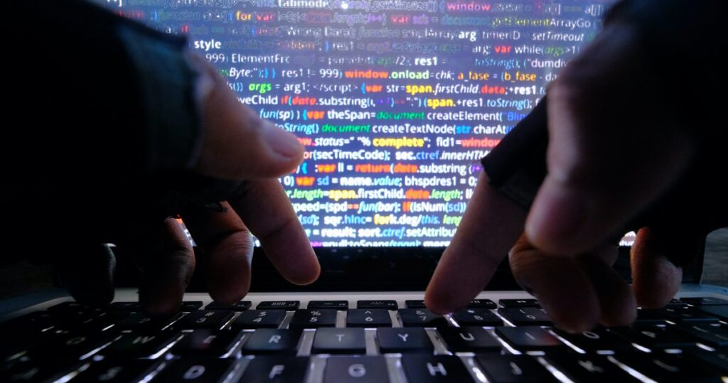An image of hands typing on a keyboard set against a backdrop of a computer screen.