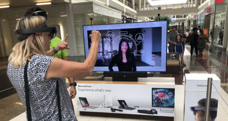A Microsoft retail employee demonstrates HoloLens's pinch-to-select gesture during a shopping mall demo.